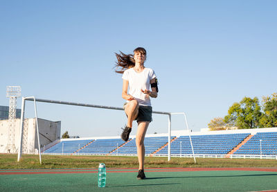 Full length of woman exercising in stadium against clear blue sky