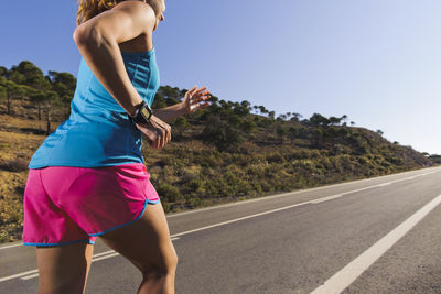 Side view of woman on road against clear blue sky