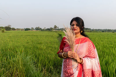 A beautiful indian woman wearing a traditional sari and jewelry stands on a paddy field background