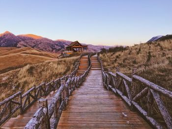 Wooden footbridge leading towards mountains against clear sky