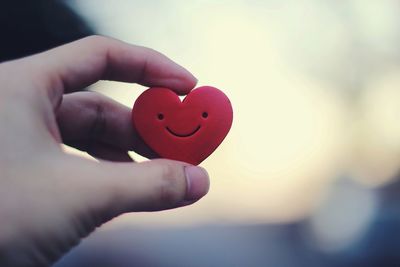 Close-up of hand holding heart shape against sky