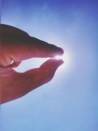 Low angle view of cropped hand against blue sky