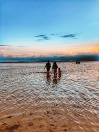 Silhouette people on beach against sky during sunset