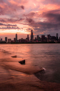 Sea by buildings against sky during sunset