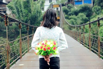Rear view of woman walking on footbridge and holding bouquet