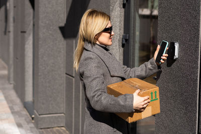 Pensive blonde woman open door using smartphone with mock up screen application, female unlocking