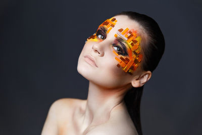 Close-up of shirtless young woman with eye make-up and rhinestones against gray background