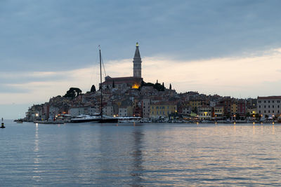 Sailboats in sea by buildings against sky in city