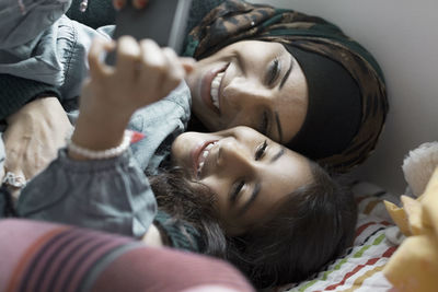 Playful mother and daughter using mobile phone in bedroom
