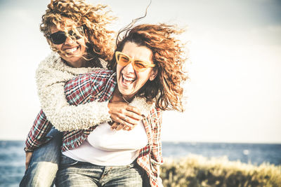 Smiling woman piggybacking friend against sky