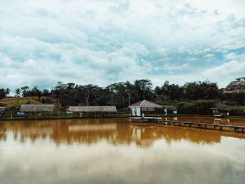 House by lake and buildings against sky