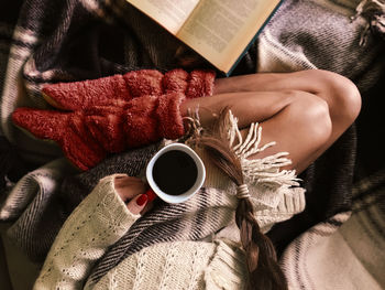 Low section of woman holding coffee cup while lying on bed