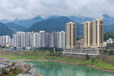 Buildings by river against sky in city