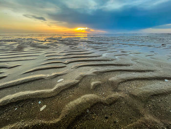 Surface level of sandy beach against sky during sunset