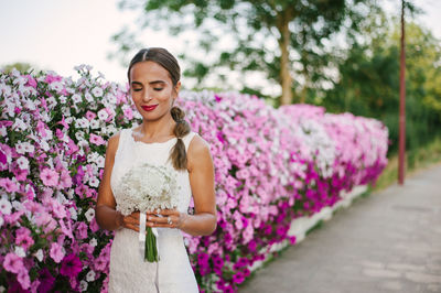 Smiling bride standing by pink flowers against sky
