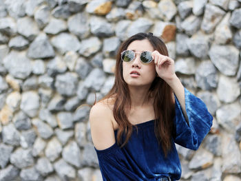 Young woman wearing sunglasses against stone wall