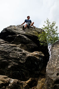Low angle view of young man sitting on cliff against sky