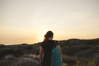 Rear view of woman standing on rock against sky during sunset