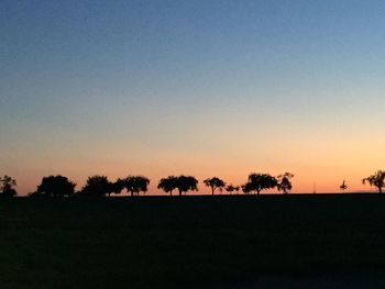 Silhouette trees on field against clear sky during sunset