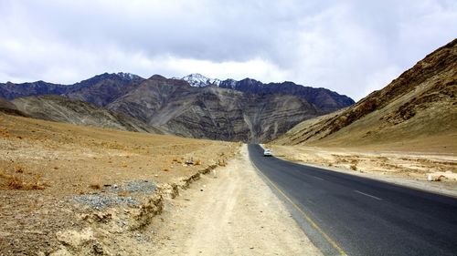 Road leading towards mountains against cloudy sky