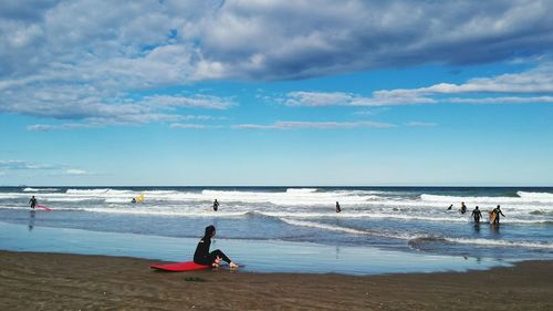 Woman sitting on surfboard at beach against sky