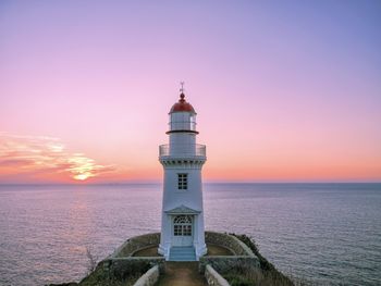 Lighthouse by sea against sky during sunset