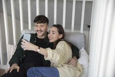 Happy young couple taking selfie on smart phone in bedroom