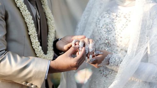 Midsection of bridegroom wearing wedding ring to bride in wedding ceremony