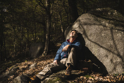 Mature man leaning on rock with eyes closed in forest