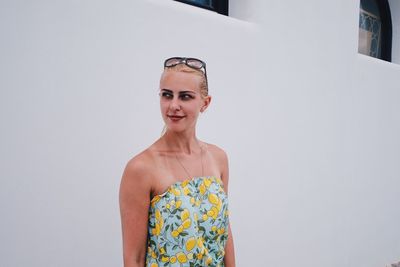 Young woman looking away while standing against wall