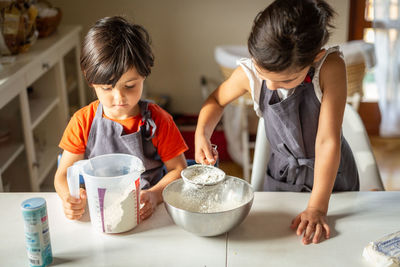 Two girls wearing grey aprons sifting flour