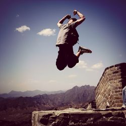 Low angle view of woman standing on mountain against sky