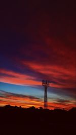 Silhouette of electricity pylon on land against sky during sunset