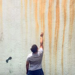 Rear view of man with arm raised standing by wall