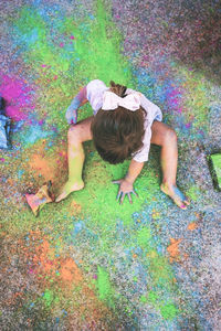 High angle view of girl playing with colorful powder paint while sitting on road