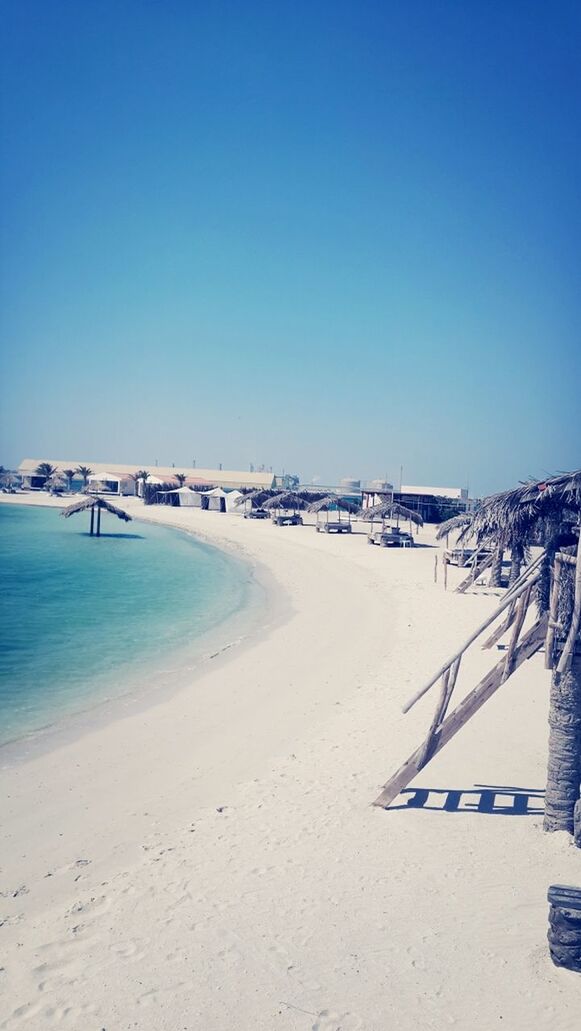 beach, clear sky, sand, sea, copy space, blue, water, shore, tranquility, tranquil scene, nature, built structure, sunlight, scenics, incidental people, architecture, day, beauty in nature, building exterior, horizon over water