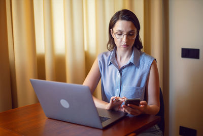 Portrait of a woman with glasses a freelancer with a laptop sitting at a table in an apartment