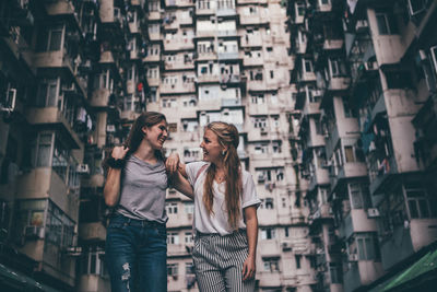 Smiling friends standing against building in city