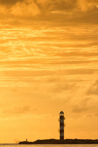 Lighthouse at coastline against orange sky during sunset