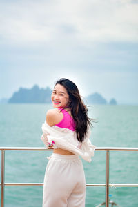 Side view of young woman standing by railing against sea