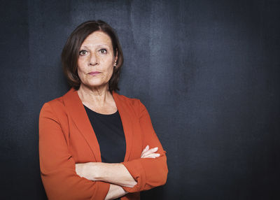 Portrait of mature businesswoman standing arms crossed against wall
