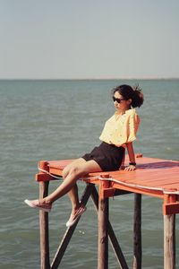 Woman sitting on sea against clear sky