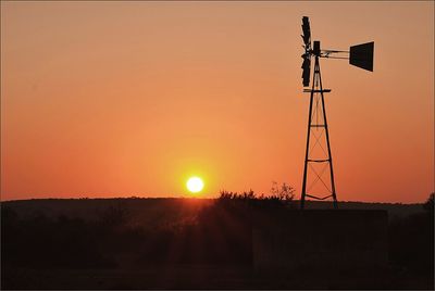 Silhouette windmill on field against orange sky