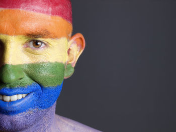 Close-up portrait of smiling man with rainbow flag body paint against black background
