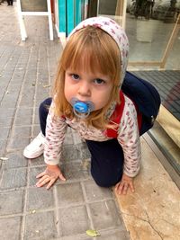 Portrait of cute girl sucking pacifier while kneeling on walkway