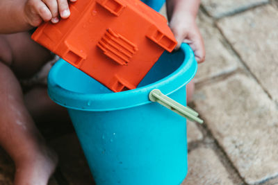 Low section of boy playing with bucket while sitting outdoors