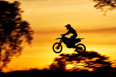 Silhouette man riding bicycle against orange sky
