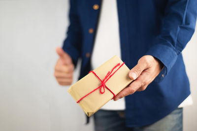 Midsection of man holding paper while standing against white wall