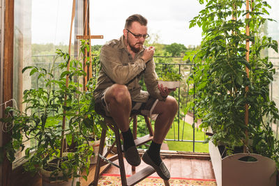 Young man sitting on chair against plants