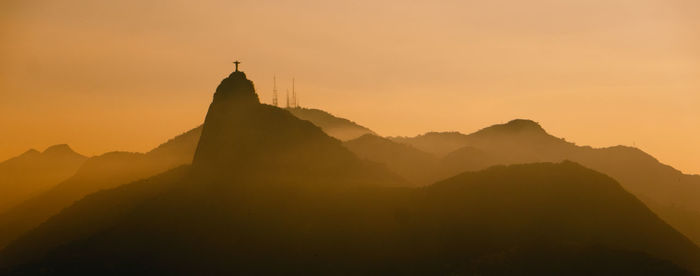 Distant view of silhouette christ the redeemer against orange sky